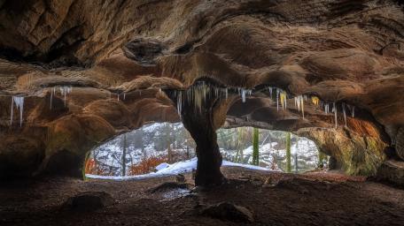 Mystical Cave with Icicles and Lush Nature Views wallpaper