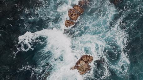 Waves Crashing Over Rugged Rocks in Turquoise Waters wallpaper