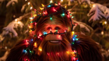 Festive Bigfoot Wrapped in Christmas Lights in a Snowy Forest wallpaper
