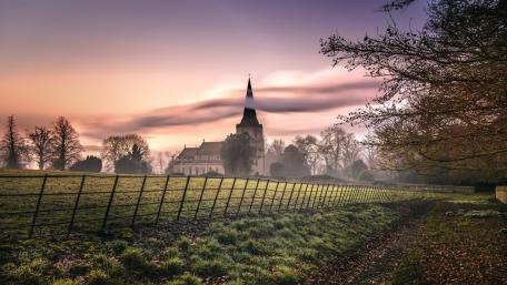 Misty Sunrise Over a Countryside Church Beyond Quiet Fields wallpaper