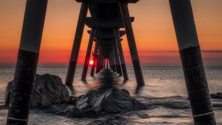 Sunset Afterglow Beneath the Pier Over Calm Ocean Rocks wallpaper