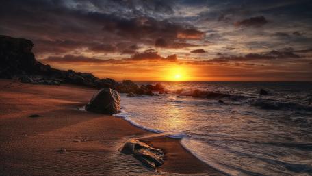 Golden Sunset Over Boulder Strewn Shoreline and Gentle Surf wallpaper