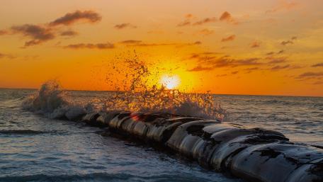 Golden Sunset Waves Crashing Over a Sea Breakwater in 4K wallpaper