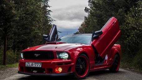 Red Ford Mustang Muscle Car with Vertical Doors in Forest Road wallpaper