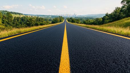 Endless Asphalt Highway Through Green Hills Toward Distant Skyline wallpaper