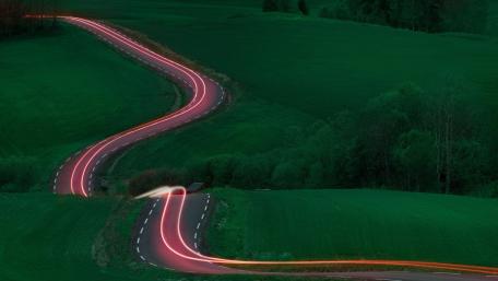 Winding Dusk Road Through Rolling Green Hills With Light Trails wallpaper