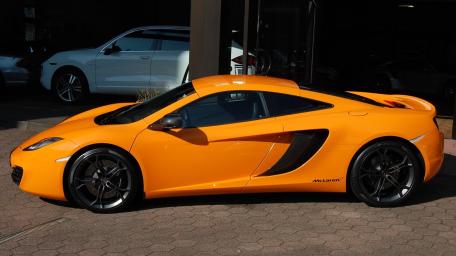 Sunlit Orange McLaren Coupe Profile in Urban Showroom Shadow wallpaper