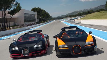 Twin Bugatti Veyron Supercars Racing Along a Sunlit Track wallpaper