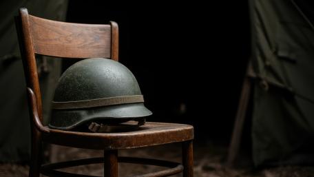 Silent Duty Helmet Resting on a Wooden Chair in Shadowed Camp wallpaper